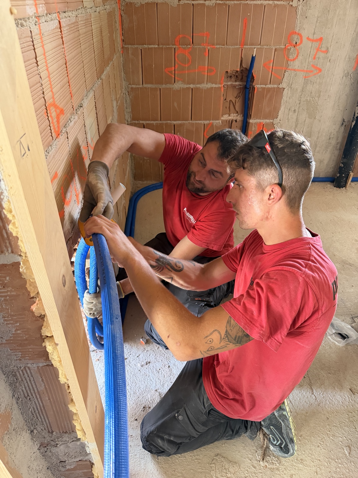 Due tecnici posano le tubazioni di un impianto in un cantiere ancora grezzo