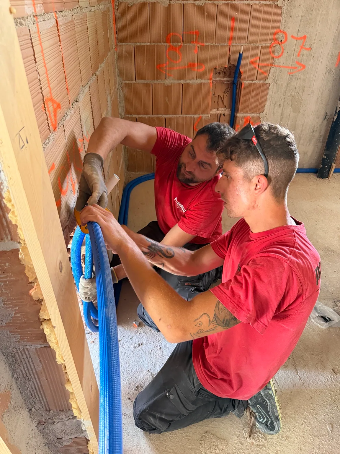 Due tecnici posano le tubazioni di un impianto in un cantiere ancora grezzo